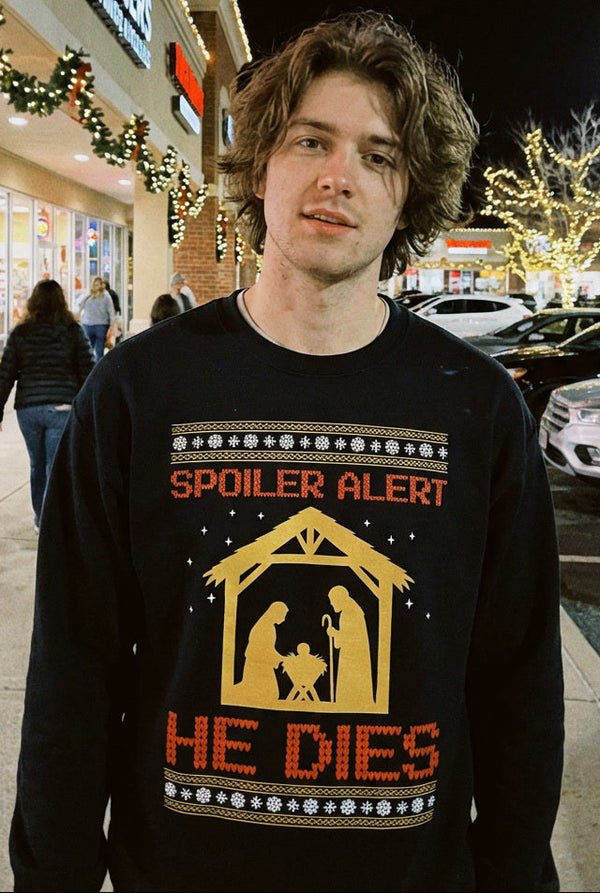 Person wearing a black sweater with a nativity scene design in a shopping mall at night.
